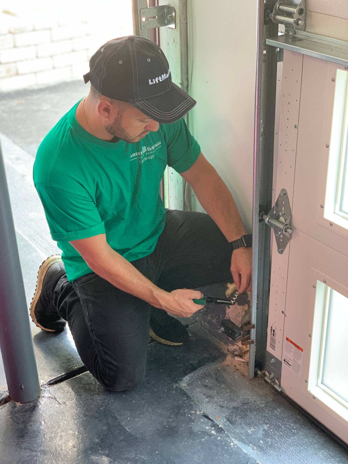 Green Garage Door Repair technician working at the base of a residential garage door track